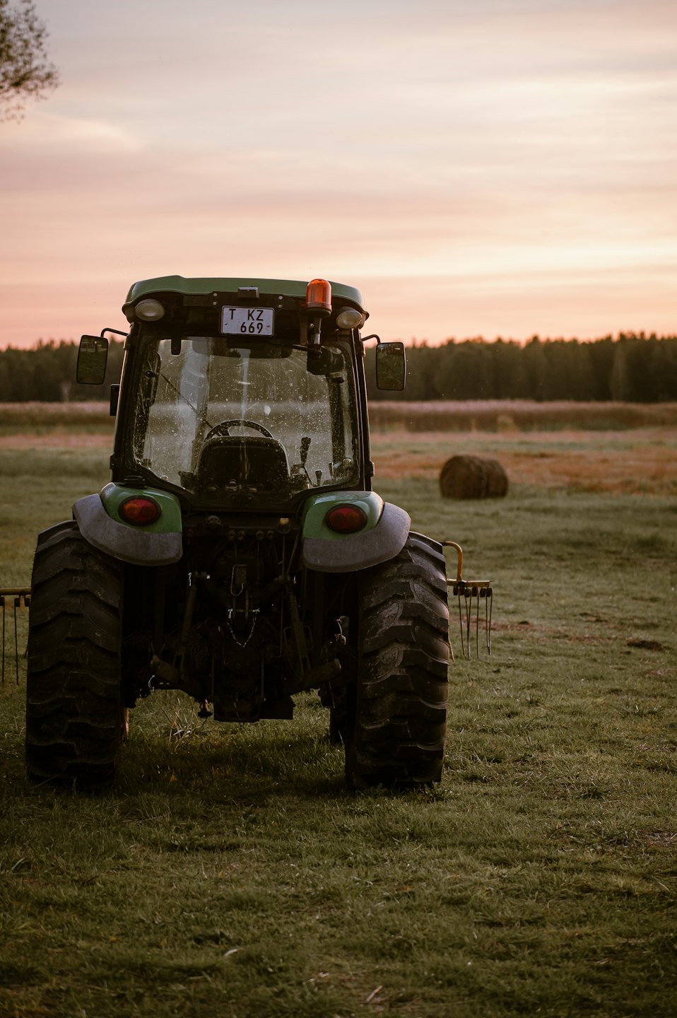 Zielony traktor zaparkowany na polu o zachodzie słońca.